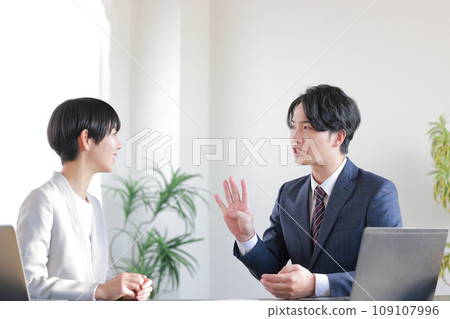 A businessman says, "There are four ways to do it," and a businesswoman smiles while listening.1 A businessman says, "There are four ways to do it," and a businesswoman smiles while listening.1 109107996