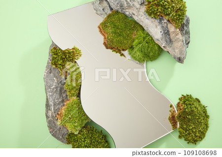 A geometric shape of mirror sheet displayed with green moss and block of gray stone on light green background. Top view, blank space for display product. Creative scene for advertising 109108698