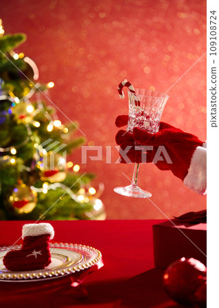 Hand model wearing santa claus gloves holding a wine glass. A dish with woolen sock featured. Christmas Day is celebrated religiously by a majority of Christians 109108724