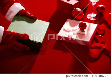 Gift boxes, ribbons and red baubles displayed on red table, a hand model with gloves id holding a box. Christmas Day is a public holiday in many countries 109108728