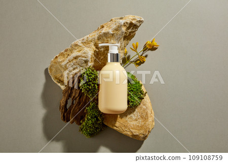 A yellow pump bottle mockup for cosmetic placed on blocks of stone with yellow flower and green moss on gray background. Minimal concept for advertising. Top view  109108759