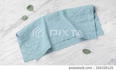Blue linen napkin folded on marble kitchen table with green leaves, top view 109109120