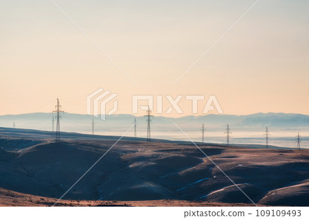 High voltage electric pole on mountain hill among remote wilderness in the sunrise at rural scene of Altai region. High voltage electric pole on mountain hill among remote wilderness in the sunrise at rural scene of Altai region. 109109493