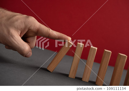 Domino has Fallen in a Row. Domino theory. Effect. Hand with Finger is Pointing and Pushing the Falling Wood Blocks. Risk Management, Revolution Concept. Affect Business. Closeup. Manifestation. Red 109111134