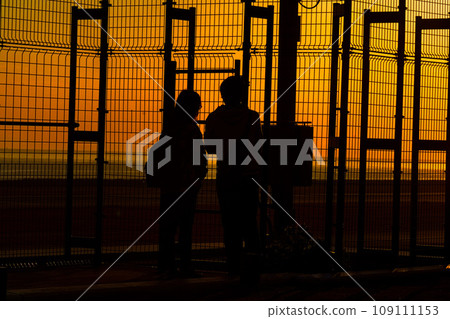 Couple silhouette watching the sunset at a seaside park 109111153