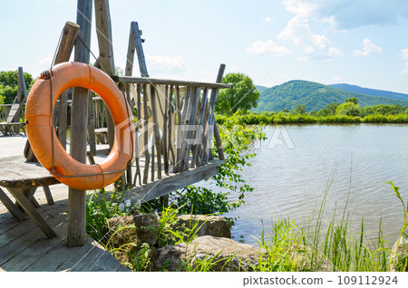 Orange life buoy hanging on the pier near the pond on a sunny summer day 109112924