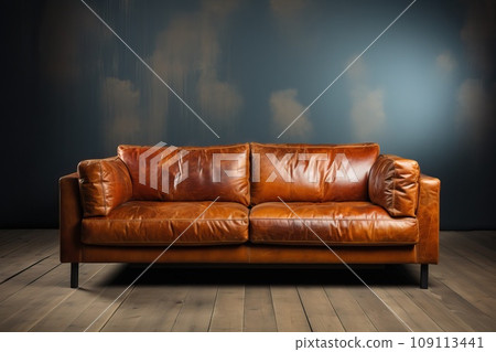 A brown leather sofa in a room with a gray wall and a brown floor. 109113441