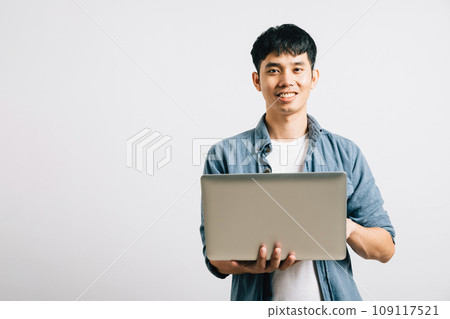 Portrait of a man with a confident smile, typing on a laptop for a successful email or chat session. Studio shot of Asian student isolated on white, showcasing his proficiency in online communication. 109117521