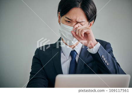 A young male office worker has itchy eyes and rubs them with his fingers 109117561