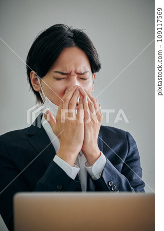 A male office worker wearing a mask covering his mouth with his hands A male office worker wearing a mask covering his mouth with his hands 109117569