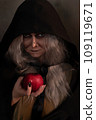 Stepmother witch gives poisoned red apple.Woman as witch in black offers red apple as symbol of temptation, poison. Fairy tale, white snow wizard concept. Spooky Halloween, cosplay. 109119671