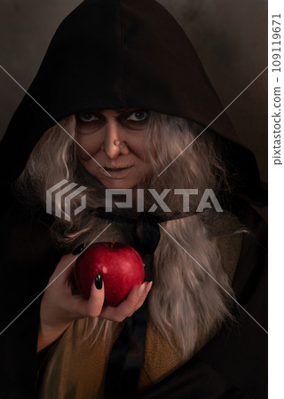 Stepmother witch gives poisoned red apple.Woman as witch in black offers red apple as symbol of temptation, poison. Fairy tale, white snow wizard concept. Spooky Halloween, cosplay. 109119671