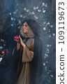 Stepmother witch gives poisoned red apple.Woman as witch in black offers red apple as symbol of temptation, poison. Fairy tale, white snow wizard concept. Spooky Halloween, cosplay. 109119673