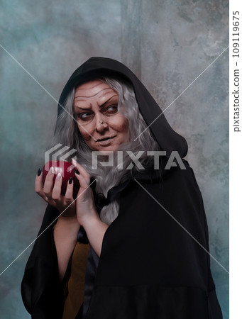 Stepmother witch gives poisoned red apple.Woman as witch in black offers red apple as symbol of temptation, poison. Fairy tale, white snow wizard concept. Spooky Halloween, cosplay. 109119675