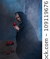 Stepmother witch gives poisoned red apple.Woman as witch in black offers red apple as symbol of temptation, poison. Fairy tale, white snow wizard concept. Spooky Halloween, cosplay. 109119676