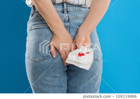 Woman holding toilet paper with blood stain on light blue background, closeup. Hemorrhoid concept Woman holding toilet paper with blood stain on light blue background, closeup. Hemorrhoid concept 109119866