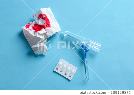 Anoscope, suppositories and toilet paper with blood on light blue background, flat lay. Hemorrhoid treatment 109119875