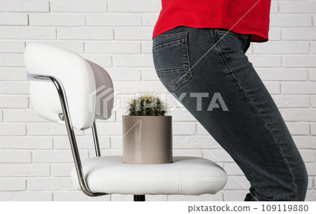 Woman sitting down on chair with cactus near white brick wall, closeup. Hemorrhoids concept 109119880