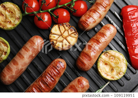 Cooking delicious fresh sausages with vegetables on modern grill, flat lay 109119951