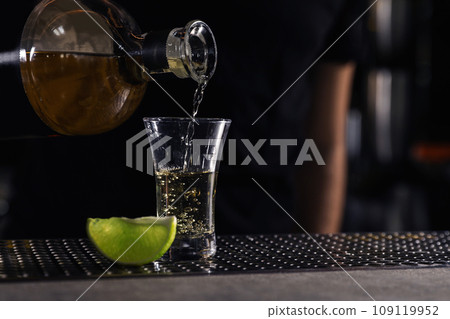 Bartender pouring Mexican Tequila into shot glass on bar counter, closeup. Space for text 109119952