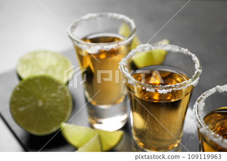 Mexican Tequila shots with salt and lime slices on grey table, closeup 109119963