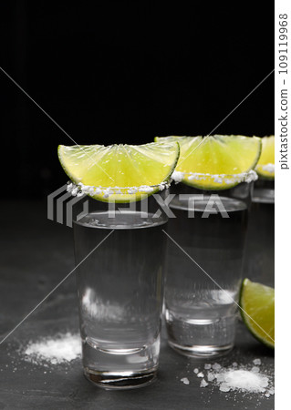 Mexican Tequila shots, lime slices and salt on black table Mexican Tequila shots, lime slices and salt on black table 109119968