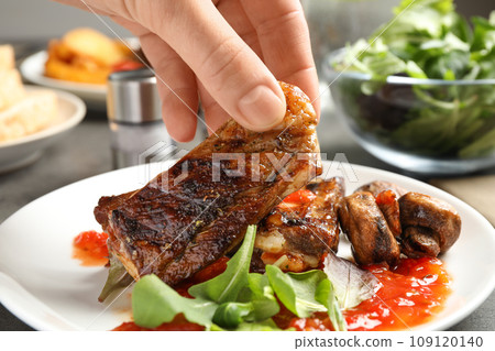 Woman with tasty grilled ribs at table, closeup Woman with tasty grilled ribs at table, closeup 109120140