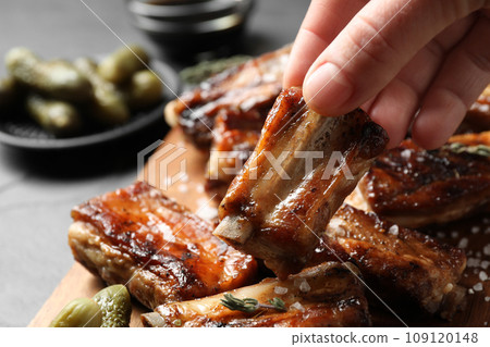 Woman with tasty grilled ribs at table, closeup Woman with tasty grilled ribs at table, closeup 109120148