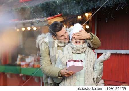 Man presenting Christmas gift to his girlfriend at winter fair Man presenting Christmas gift to his girlfriend at winter fair 109120469