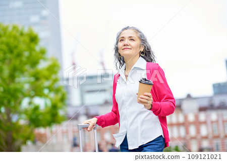 Senior woman holding a suitcase while drinking coffee 109121021