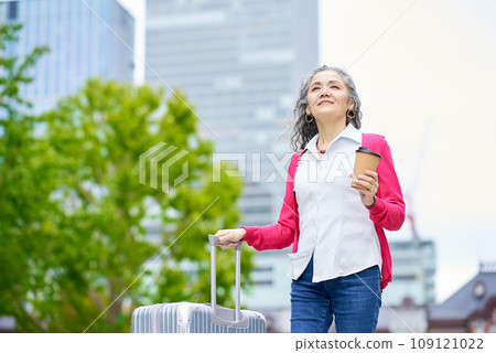 Senior woman holding a suitcase while drinking coffee Senior woman holding a suitcase while drinking coffee 109121022