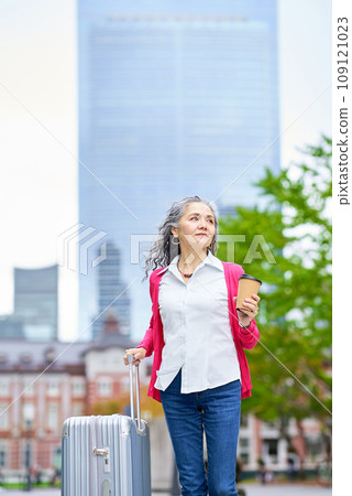 Senior woman holding a suitcase while drinking coffee Senior woman holding a suitcase while drinking coffee 109121023