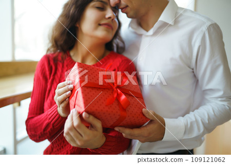 A young man gives his beloved a present and closes her eyes with a hand. Valentine's Day. 109121062