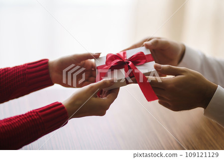 Man gives to his woman a gift box with red ribbon. Hands of man gives surprise gift box for girl. 109121129