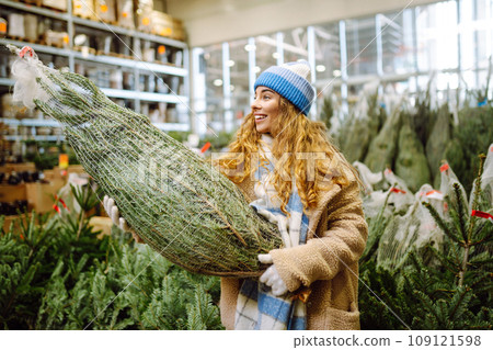 Beautiful young woman buys a Christmas tree at the fair. New Year's holiday concept Beautiful young woman buys a Christmas tree at the fair. New Year's holiday concept 109121598