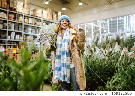 Beautiful young woman buys a Christmas tree at the fair. New Year's holiday concept Beautiful young woman buys a Christmas tree at the fair. New Year's holiday concept 109121599