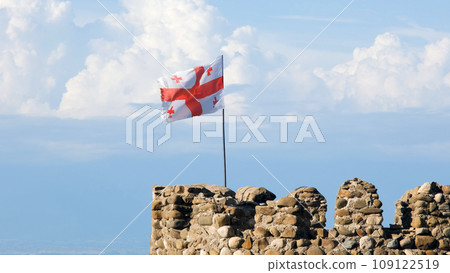 Flag of Georgia waving on the top of an old tower by the blue sky and clouds Flag of Georgia waving on the top of an old tower by the blue sky and clouds 109122519