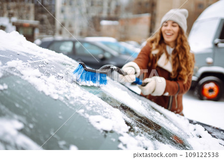 Beautiful woman is cleaning snow from a car with a brush. Transport concept, seasonality 109122538