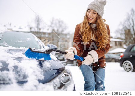 Cleaning snow from a car. Beautiful woman is cleaning snow from a car with brush. Transport concept. Cleaning snow from a car. Beautiful woman is cleaning snow from a car with brush. Transport concept. 109122541