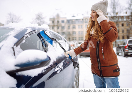 Cleaning snow from a car. Beautiful woman is cleaning snow from a car with brush. Transport concept. 109122632