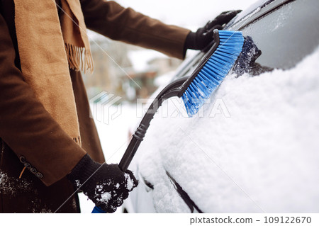 Stylish man in a coat and scarf clears snow from his car during winter snowfall. Seasonality concept 109122670
