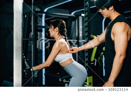 Trainer teaching proper form and technique for using a weight machine to train the biceps, helping his client achieve a stronger and healthier body. GYM healthy lifestyle concept 109123314