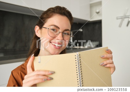 Close up portrait of young woman smiling, holding notebook, showing her planner 109123558