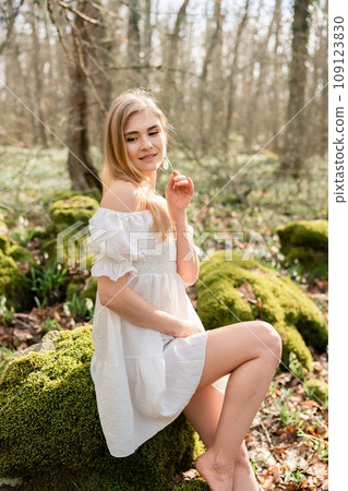 Snowdrops galanthus blonde. A girl in a white dress sits on a meadow with snowdrops in a spring forest 109123830