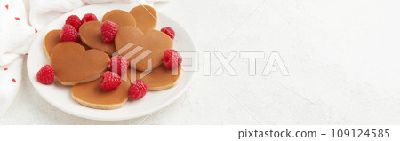 A heap of heart shaped pancakes with raspberries on the white plate on the white background 109124585