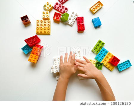 Child playing with colorful building blocks on white background. Top view 109126120