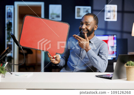 Happy man comissioned by brand to film sponsored content, holding empty copy space sign in hand, talking to audience. Trending media star using cardboard bubble speech cutout to do promotion to fans Happy man comissioned by brand to film sponsored content, holding empty copy space sign in hand, talking to audience. Trending media star using cardboard bubble speech cutout to do promotion to fans 109126268