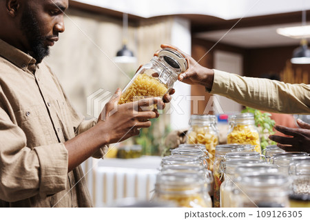 Close-up shot of an African American man checking out the pasta in the glass jars. At an environmentally conscious supermarket, a male customer looking at nutritious bulk products. Close-up shot of an African American man checking out the pasta in the glass jars. At an environmentally conscious supermarket, a male customer looking at nutritious bulk products. 109126305