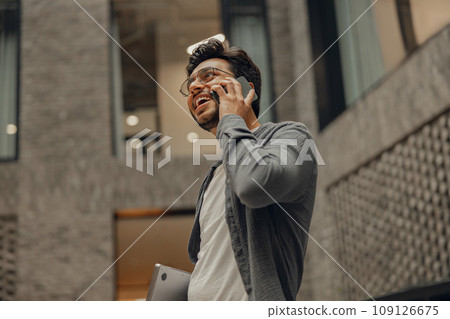 Stylish businessman in eyeglasses is talking phone standing in modern coworking space Stylish businessman in eyeglasses is talking phone standing in modern coworking space 109126675