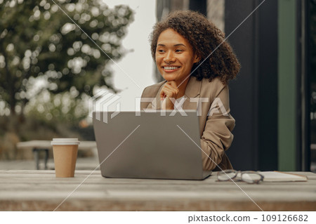 Smiling female freelancer working on laptop while sitting in cafe terrace. Distance work concept 109126682